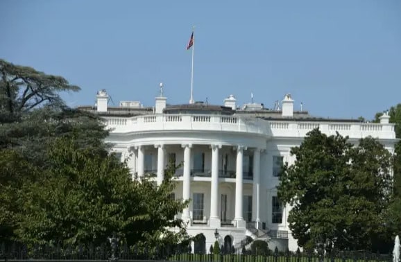 Luxurious White House with lush green trees in the foreground and clear blue sky, showcasing iconic American political architecture and grandeur.